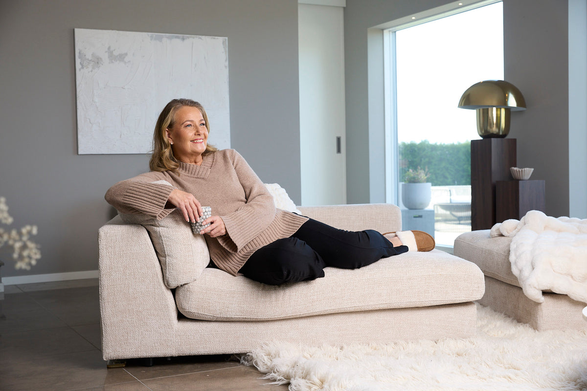 Yvonne Ryding myser i en soffa med en kopp te med en beige stickad tröja